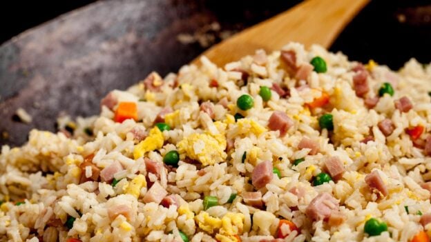 Fried rice with ham and veggies in a wok with a brown serving spoon.