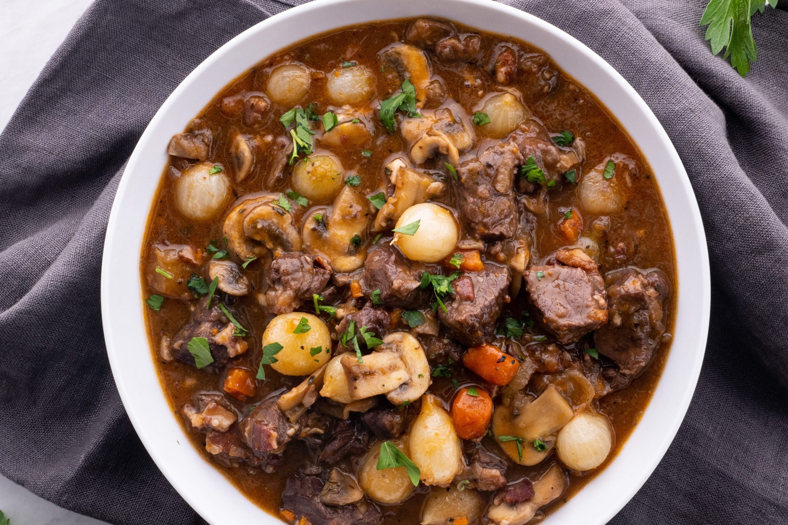 Boeuf Bourguignon in a round bowl on a grey napkin.