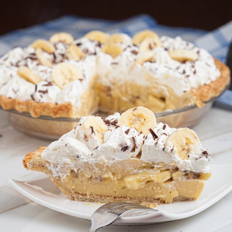 a slice of banana cream pie on a plate with the rest of the pie in the background