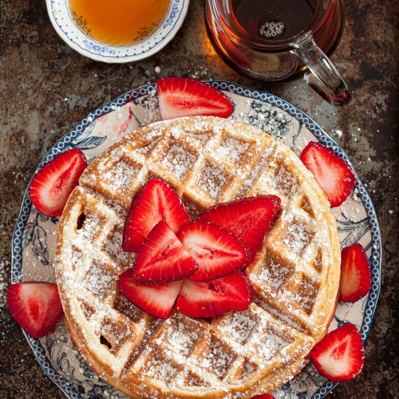 overhead image of a stack of Belgian waffles topped with powdered sugar and sliced strawberries