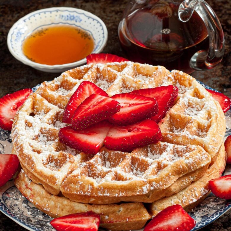 a stack of fluffy Belgian waffles topped with strawberries