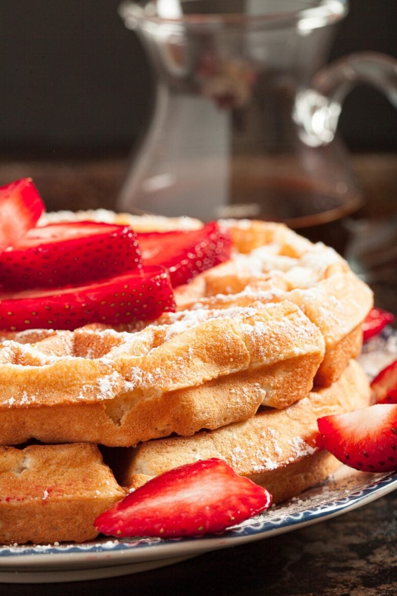 side image of a stack of Belgian waffles topped with sliced strawberries