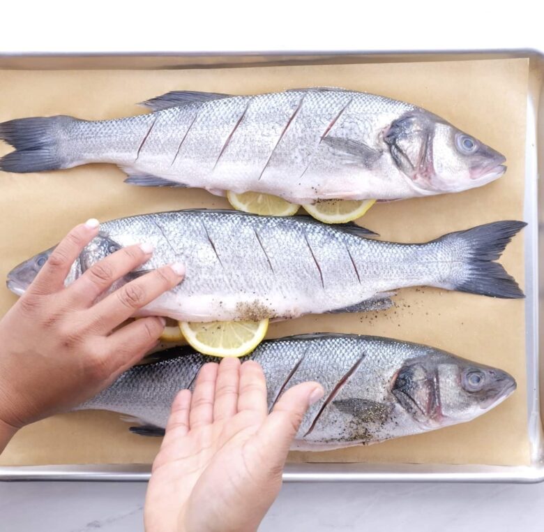 Branzino fish being seasoned with spices and lemon.