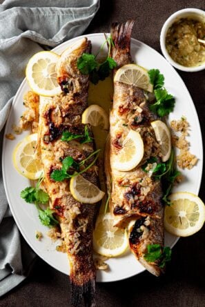 Cooked whole branzino fish with lemon slices and butter sauce.
