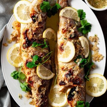 Cooked whole branzino fish with lemon slices and butter sauce.