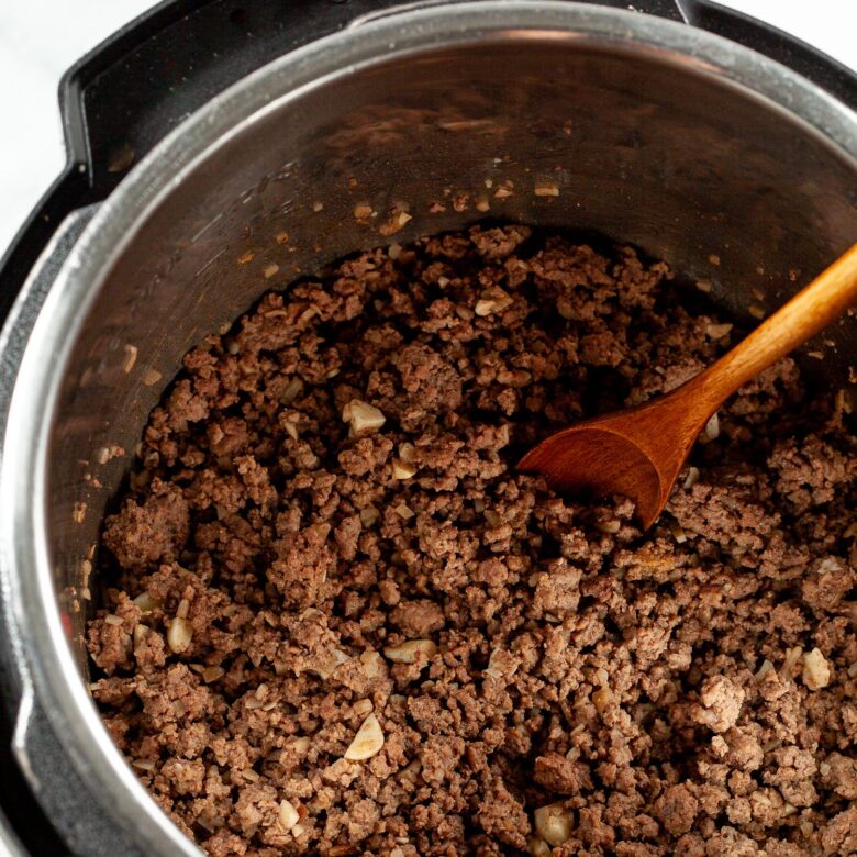 browned beef in an Instant Pot with a wooden spoon sticking out