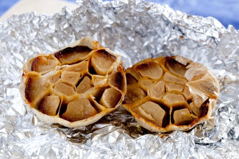 two roasted halves of a head of garlic on aluminum foil