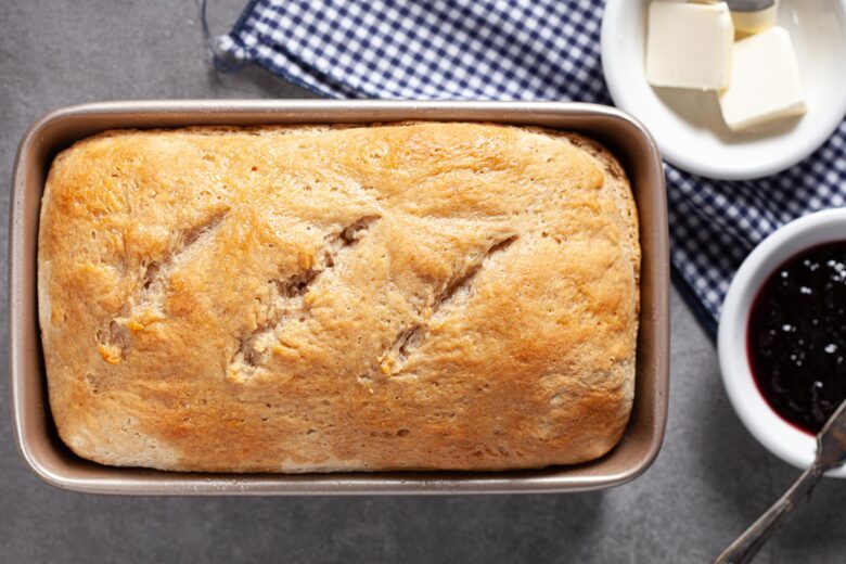 A perfectly baked loaf of sourdough sandwich bread still in the pan.