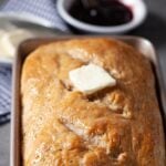 Baked sourdough bread loaf in a metal baking pan with butter on top