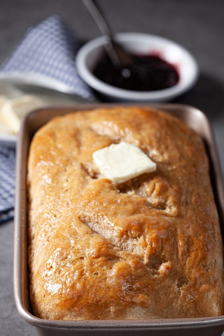 Baked sourdough bread loaf in a metal baking pan with butter on top