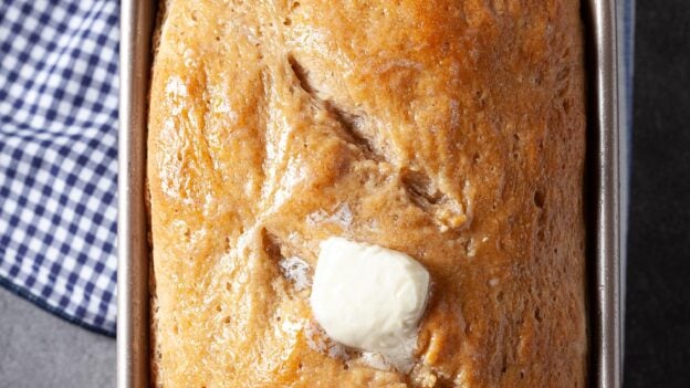 Baked sourdough bread in the pan with butter on top.