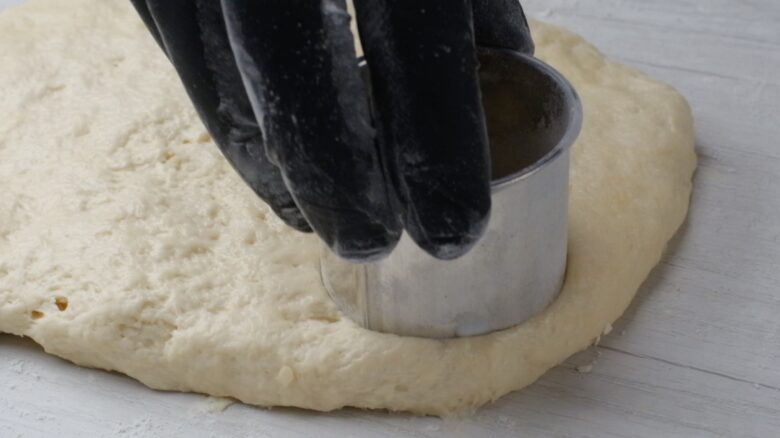 Buttermilk biscuit dough being cut into circle shape with a round biscuit cutter.