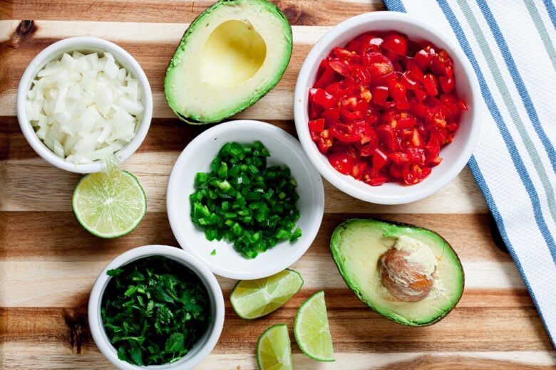 Avocado halves, onions, jalapeno, cilantro, diced tomatoes, and sliced limes for guacamole