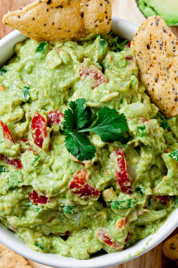 Guacamole with diced tomatoes and lime slices with tortilla chips