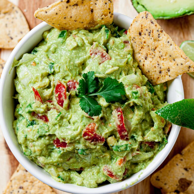 Guacamole with diced tomatoes and lime slices with tortilla chips