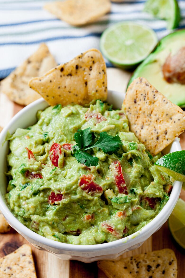 Guacamole with diced tomatoes and lime slices with tortilla chips