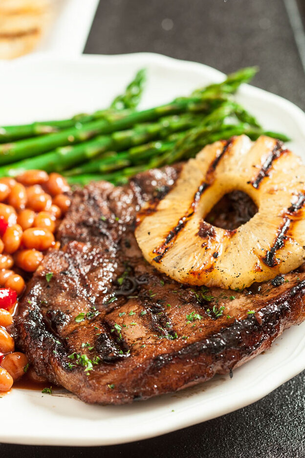 Grilled pork chops with grilled pineapple, bbq beans, and asparagus on a plate