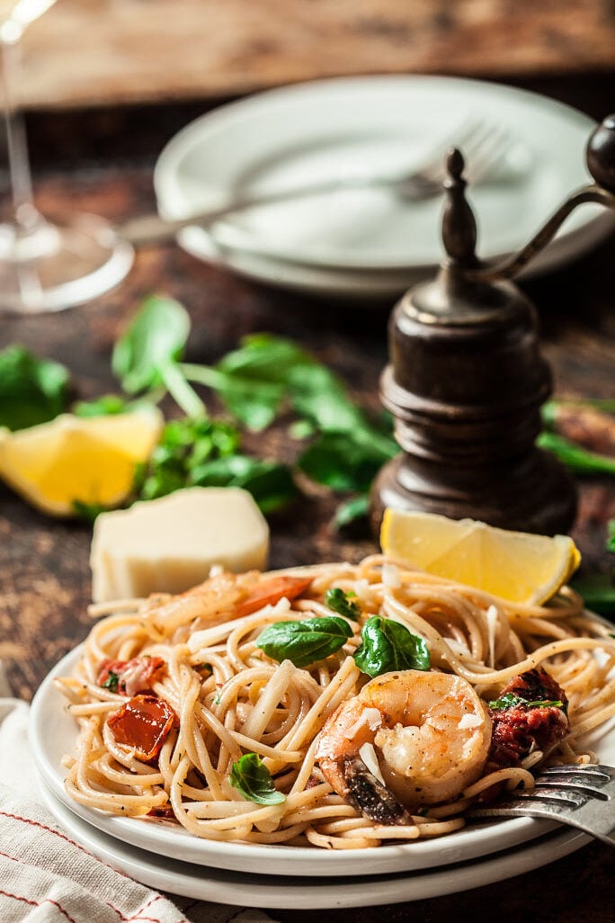Shrimp Scampi pasta with tomatoes and basil and lemon slices on a white plate