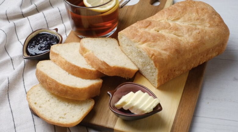 Sliced, baked sourdough sandwich bread with a dish of butter and jam on the side.