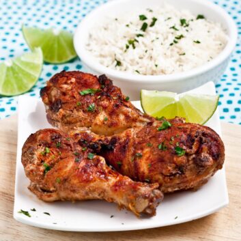 Baked Tandoori Chicken on white plate with a bowl of basmati rice on the side
