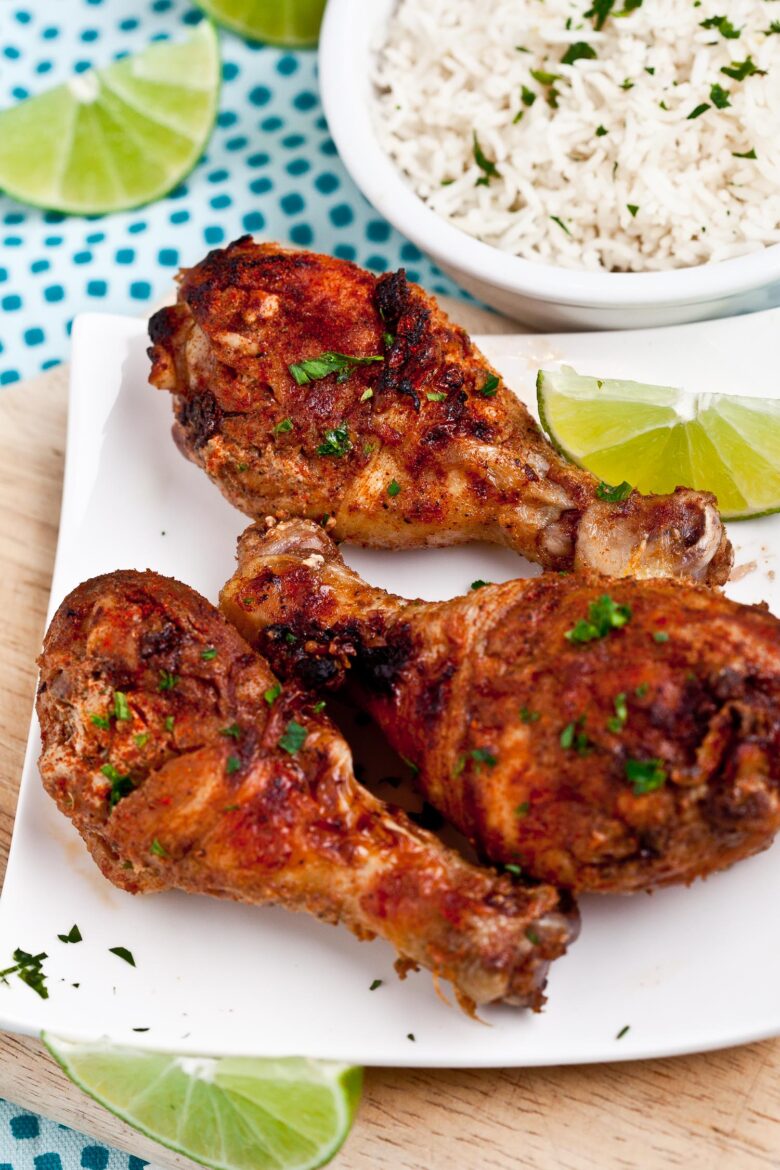 Baked Tandoori Chicken on white plate with a bowl of basmati rice on the side