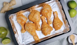 Marinated tandoori chicken on a lined baking sheet.