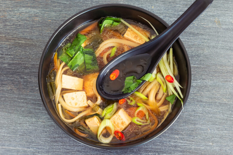 a bowl of noodles, tofu, and vegetables in soup