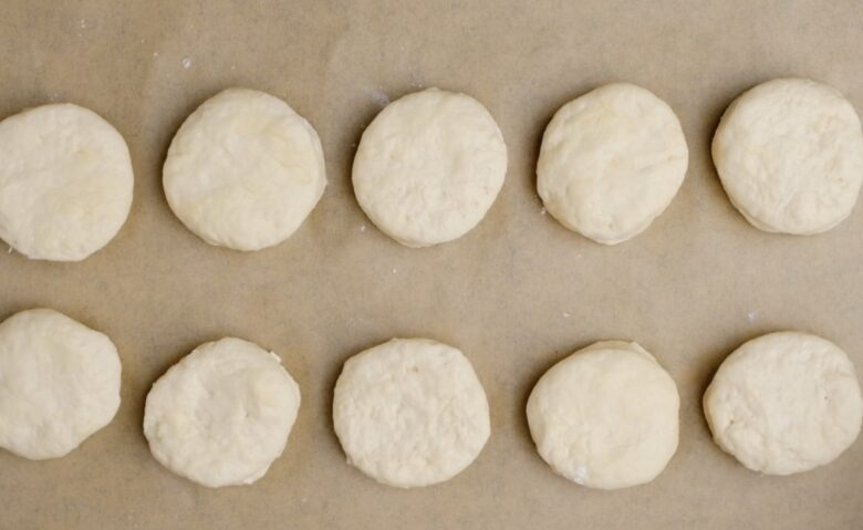 Cut biscuit dough rounds placed on a baking sheet.