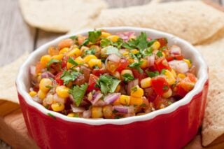 Fresh corn salsa in a bowl with tortilla chips on the side.