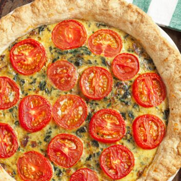 Cooked spinach quiche in the pan topped with tomatoes