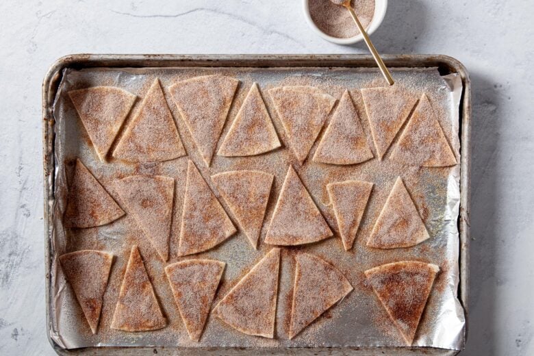 Tortilla wedges laid on a baking sheet and sprinkled with cinnamon and sugar.