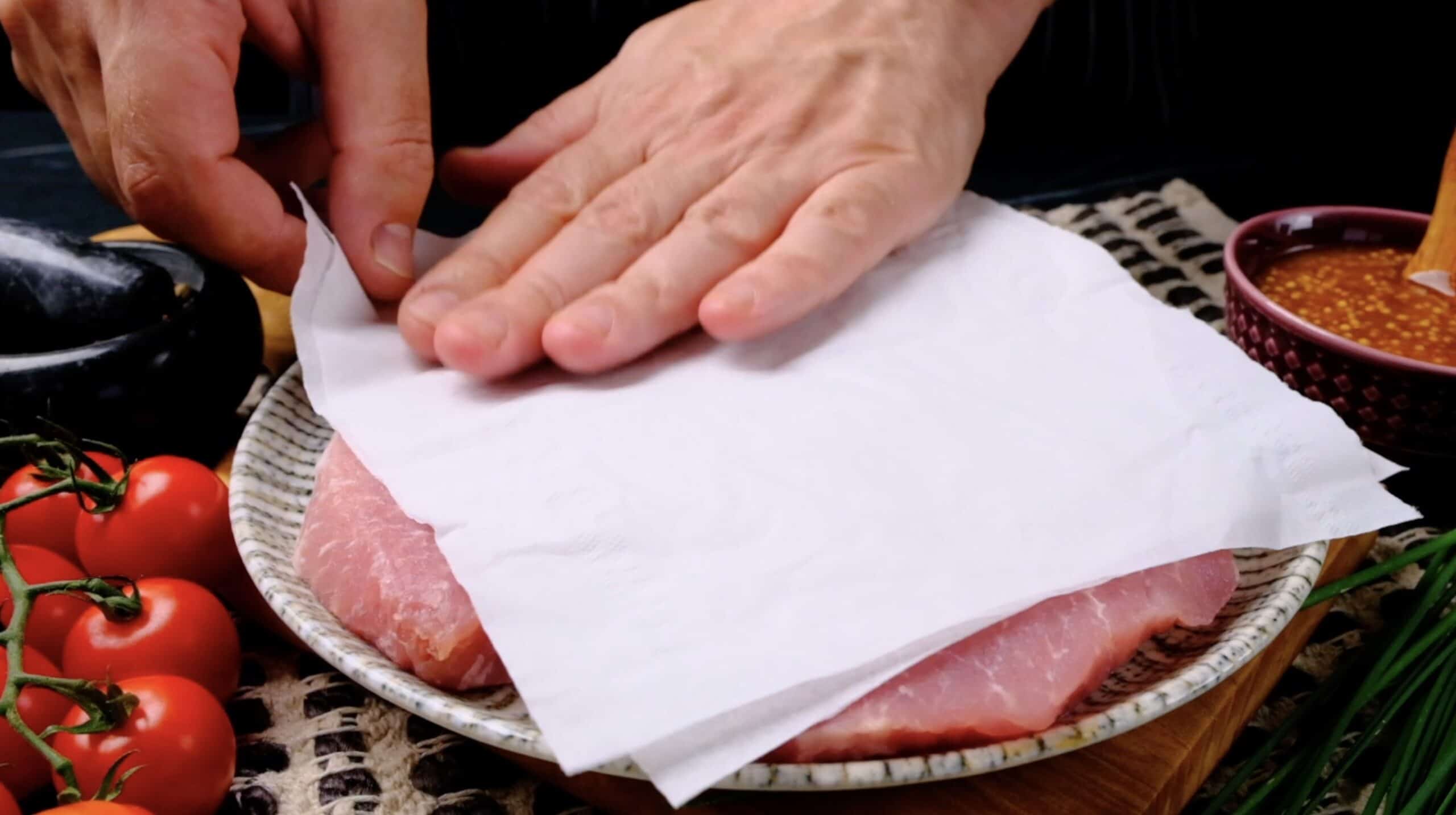 Pork chops being patted dry with paper towel.