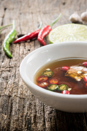 A dipping sauce made with fish sauce, chilies, and lime in a white bowl.