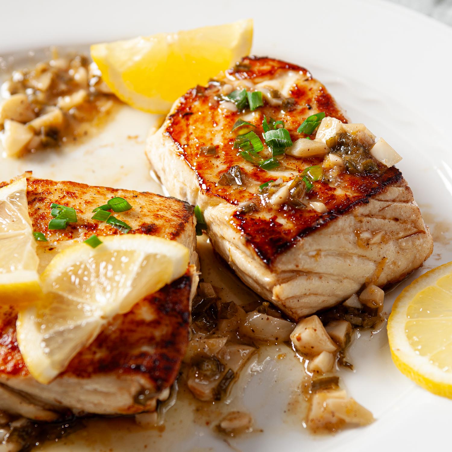 two seared halibut filets on a plate topped with lemon and garlic.