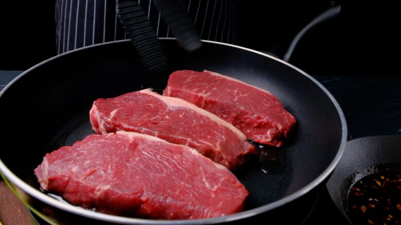 steaks cooking in pan on first side.