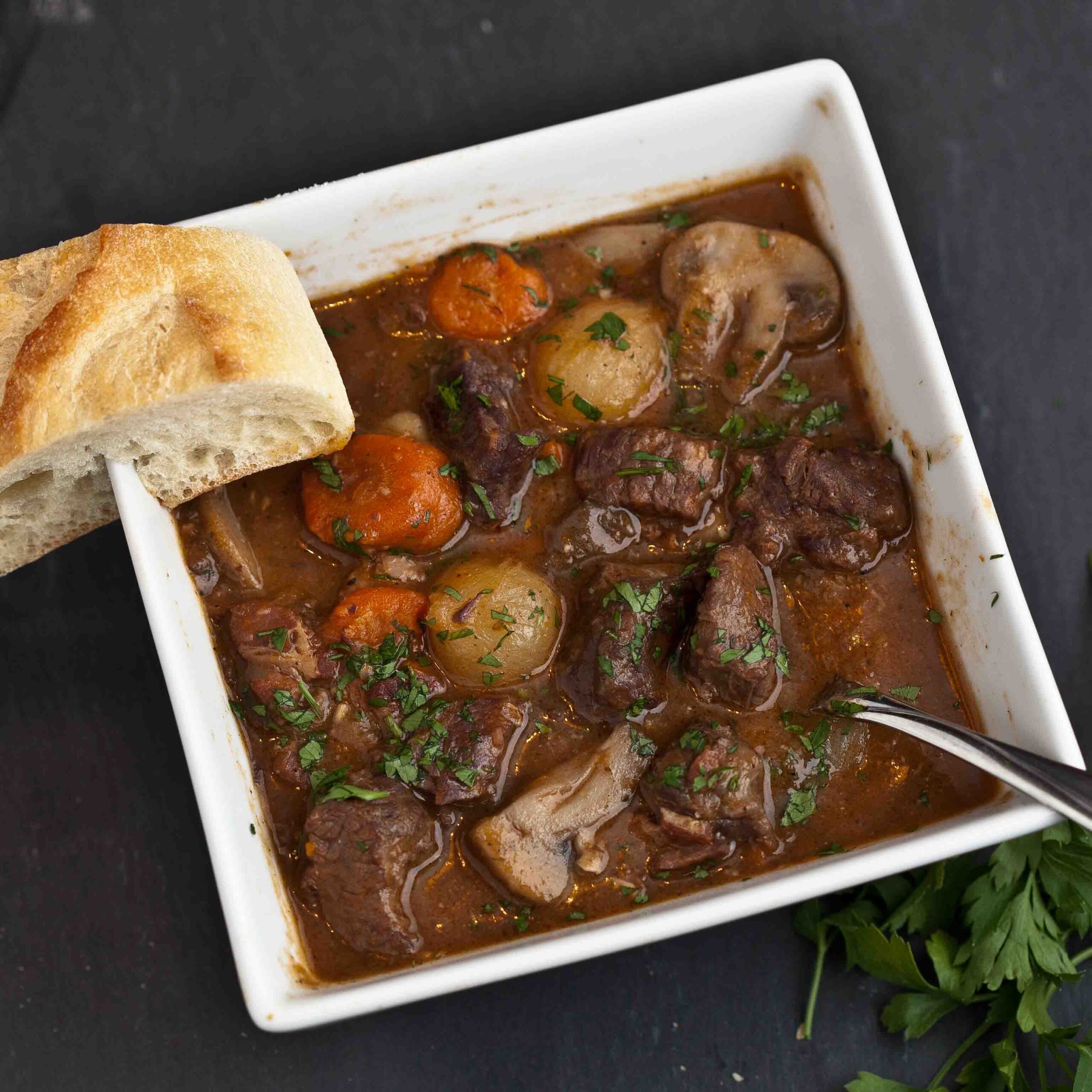 Boeuf Bourguignon in a square bowl with a slice of baguette on the rim of the bowl.