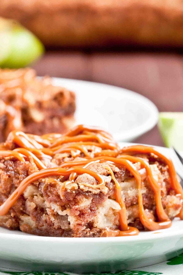 Slice of apple cake with caramel drizzle on a white plate.