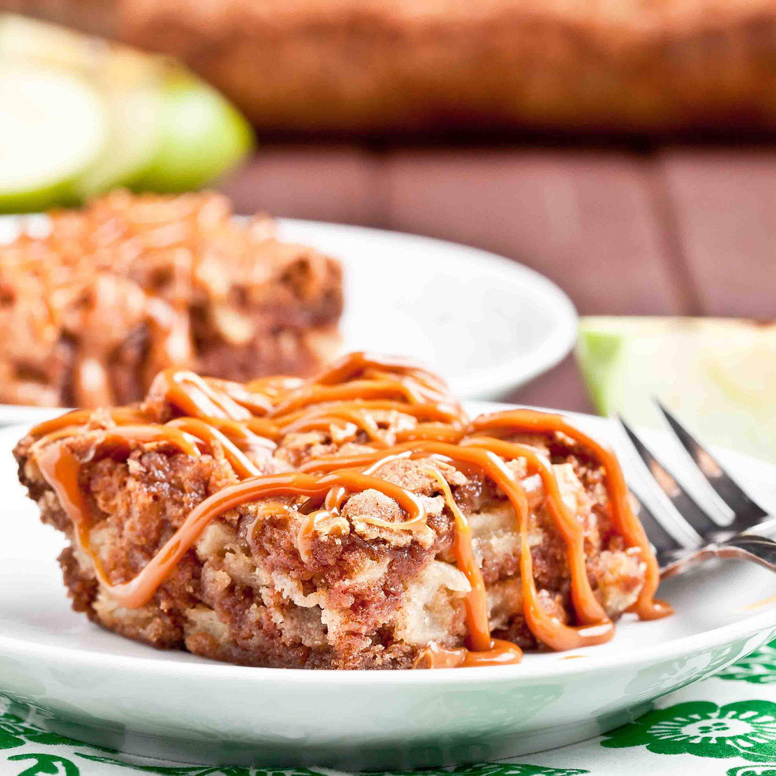 Slice of apple cake with caramel drizzle on a white plate.