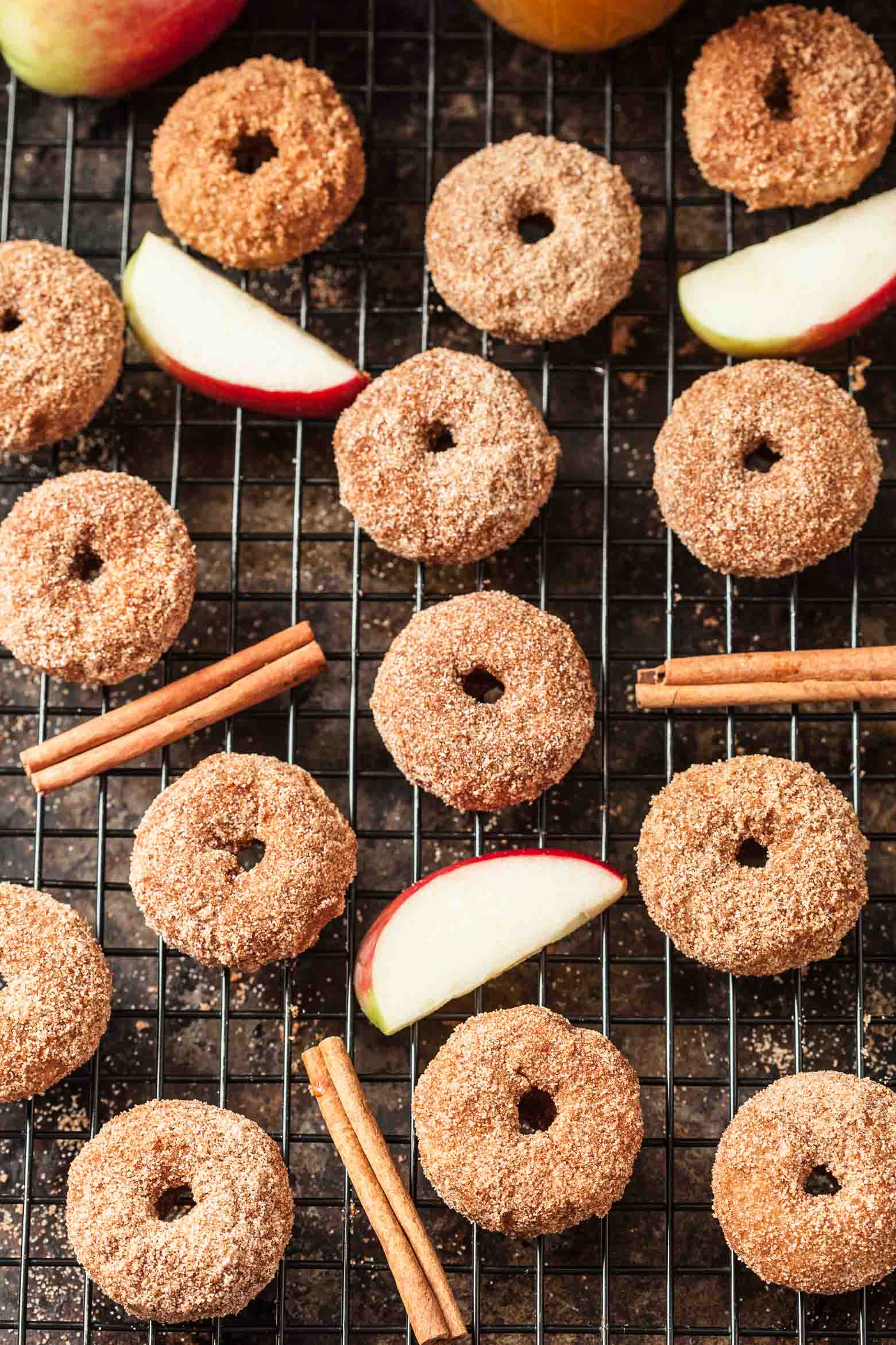 Bunch of donuts on a cooling rack with cinnamon sticks and apples in between.