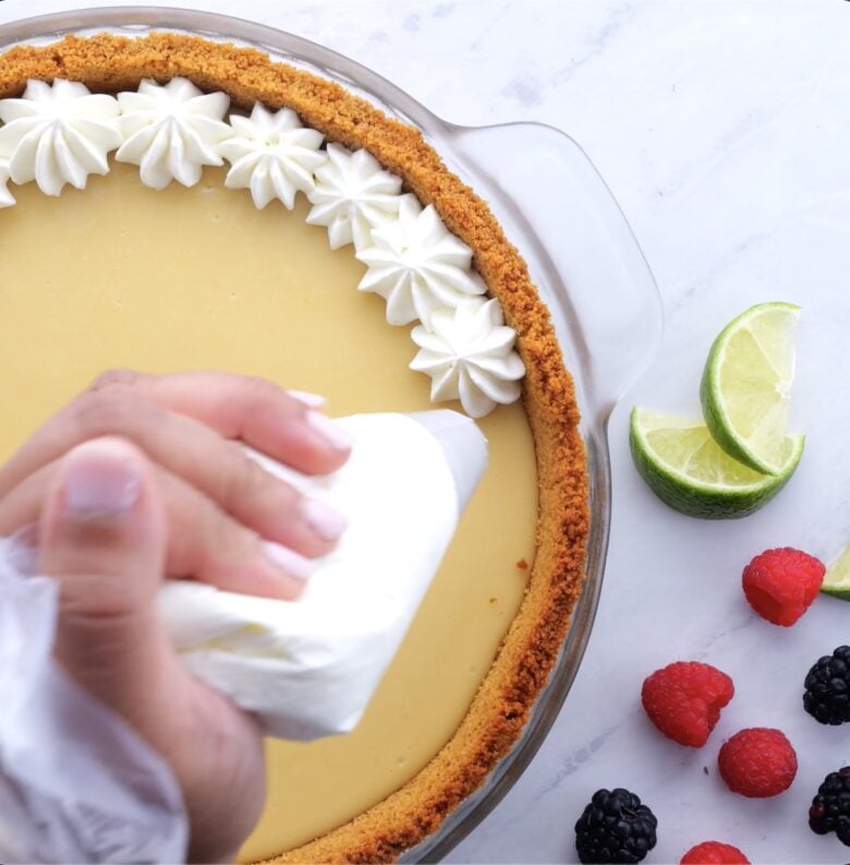key lime pie being decorated with a piping bag using whipped cream