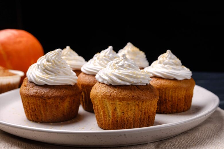 whipped cream frosting on a plate of pumpkin cupcakes. 