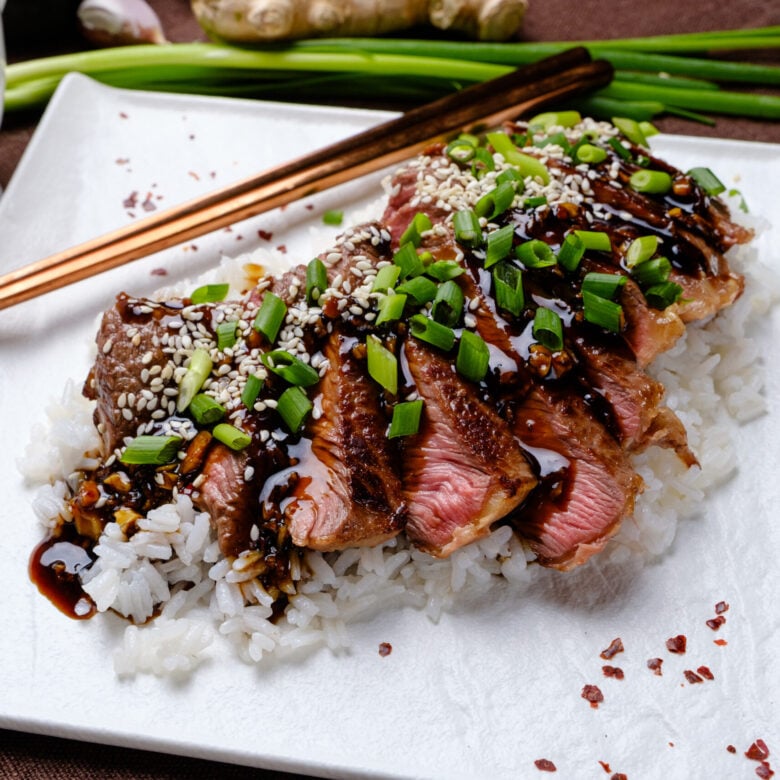 Beef Teriyaki sliced on a bed of white rice with green onions.