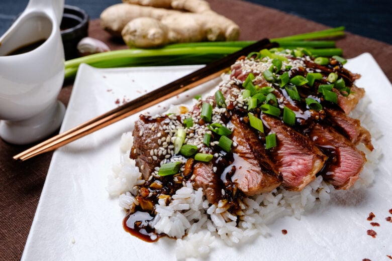 Beef Teriyaki sliced on a bed of white rice with green onions.