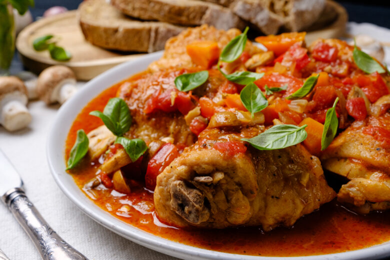 Chicken cacciatore on a plate garnished with fresh basil leaves.
