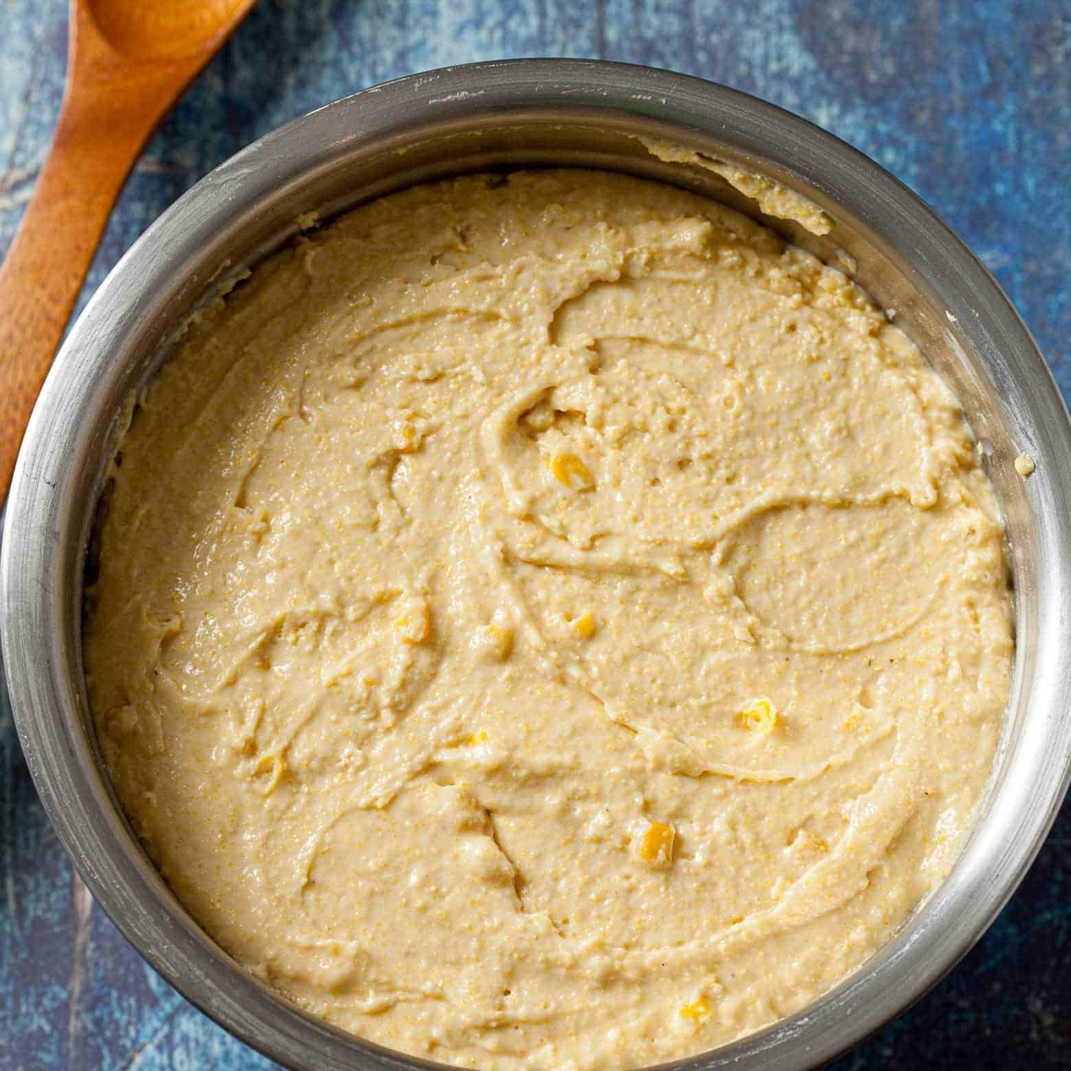 Thick honey cornbread muffin batter with corn kernels in a stainless steel mixing bowl.