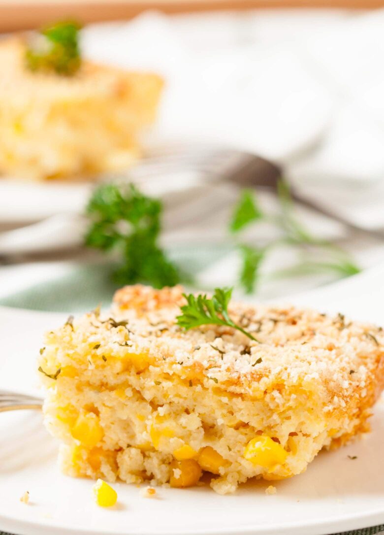 A slice of corn casserole with visible pieces of corn, placed on a white plate.