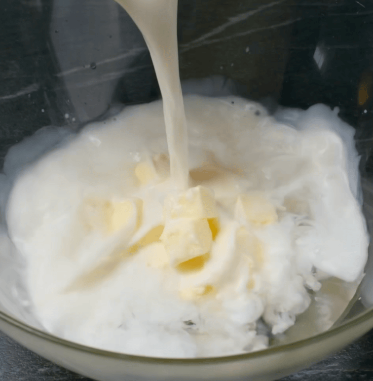 Milk being poured into a microwave-safe bowl with cubed butter already in it.
