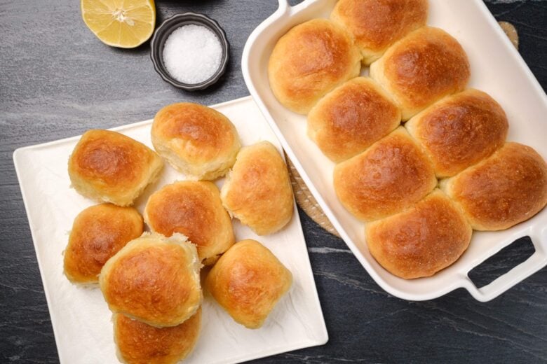 Overhead shot of easy dinner rolls in a white plate next to more dinner rolls in a white baking tray.