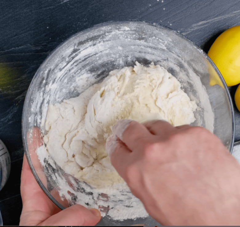 A person kneading dough in a bowl to make easy dinner rolls, with lemons in the background.