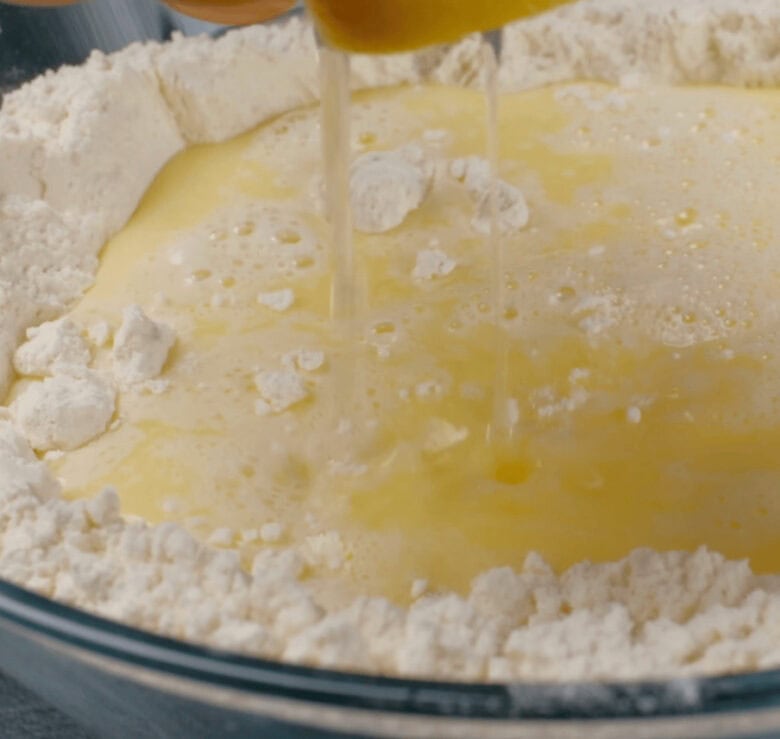 Wet ingredient mixture being poured into bowl with dry ingredient mixture of easy dinner rolls.